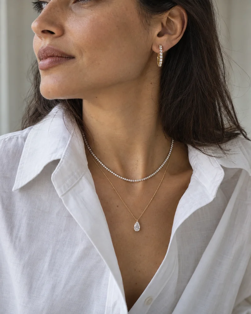 Diamond hoop earrings, a fine diamond tennis necklace and a pear diamond pendant worn with an open white cotton shirt.