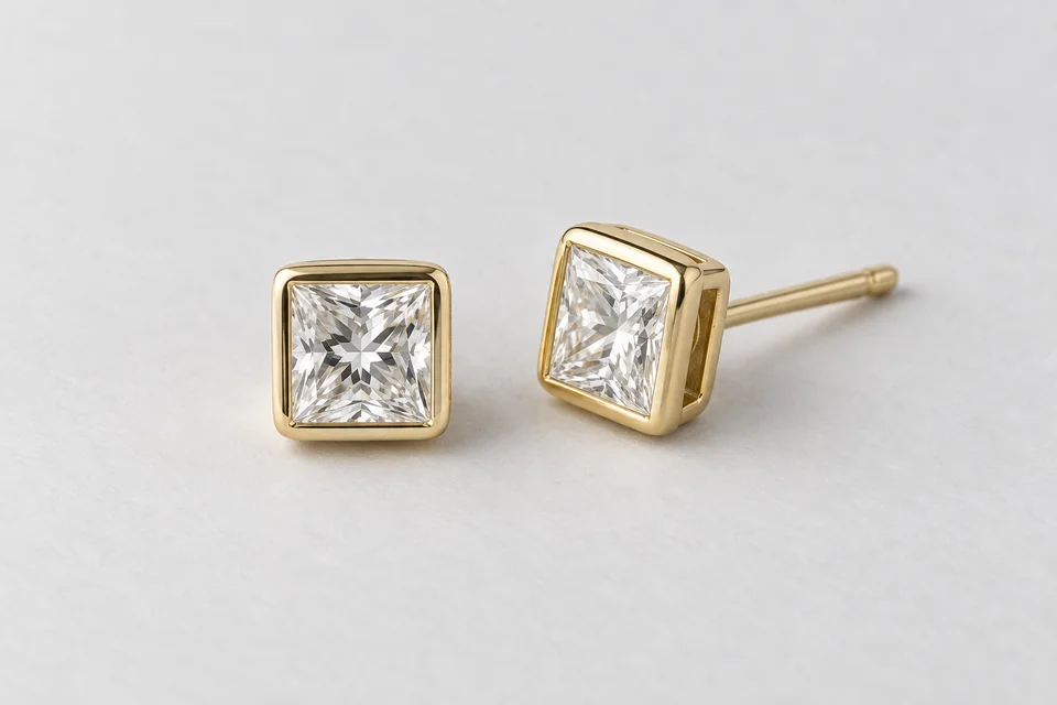 Two yellow-gold square bezel diamond studs, shown in full at gently differing angles on pale paper.