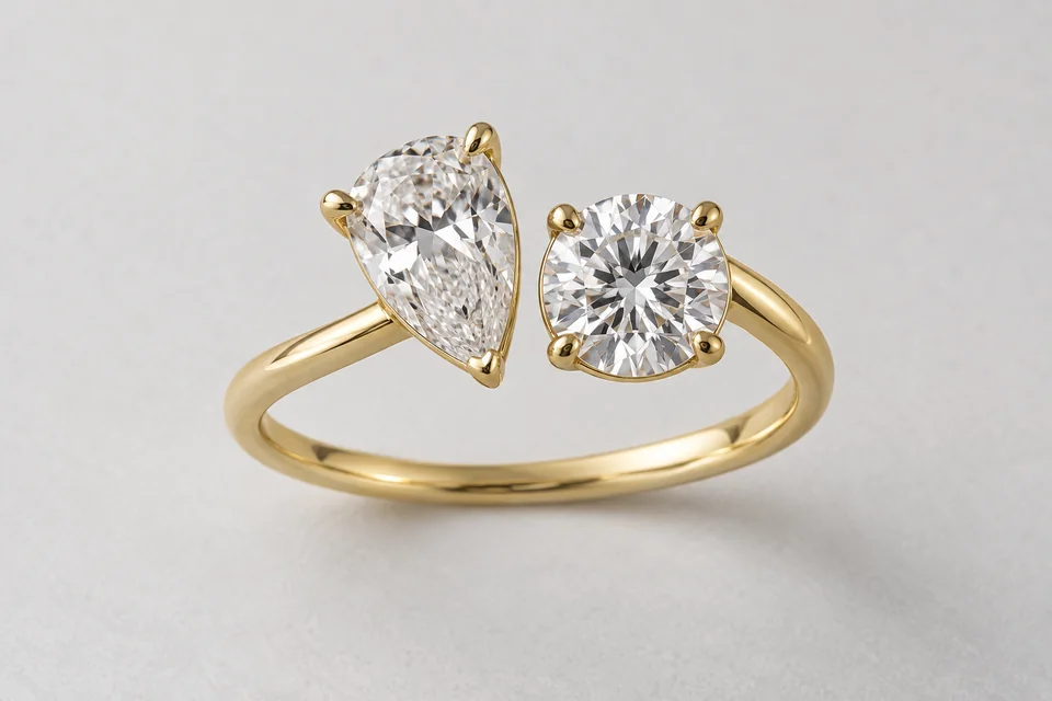 A complete yellow-gold toi-et-moi ring with a pear diamond beside a round brilliant diamond on pale paper.