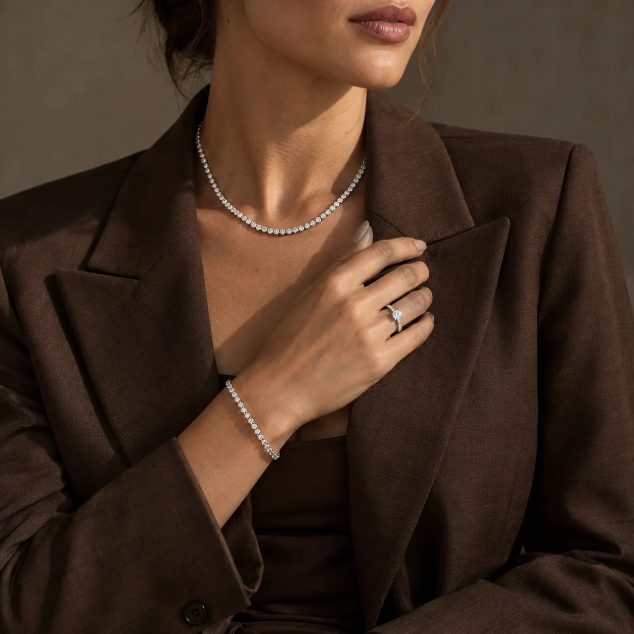 Diamond tennis necklace, solitaire ring and tennis bracelet worn with a chocolate-brown blazer.