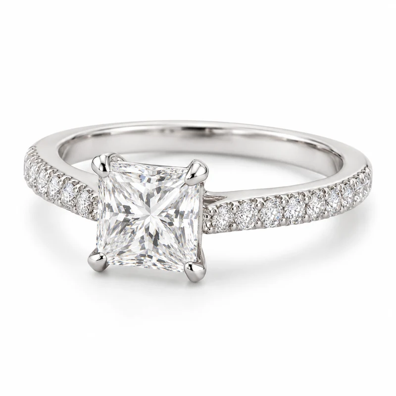 A white-gold princess-cut diamond solitaire with four corner prongs and diamond-pavé shoulders, on pure white.