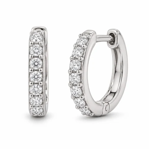 A complete pair of white-gold diamond huggie earrings on white.