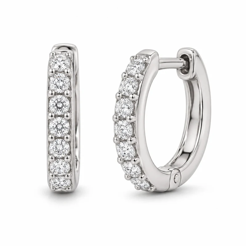 A pair of white-gold diamond huggie earrings on pure white, with complete hoops and visible diamond settings.