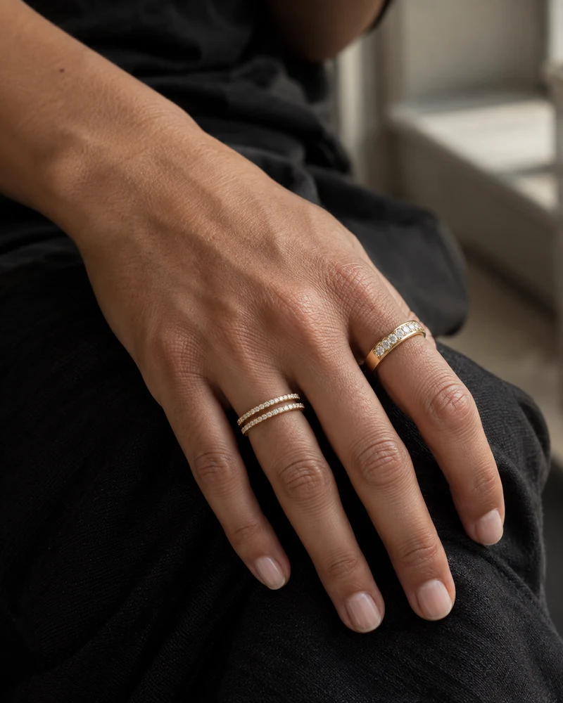 A relaxed hand wearing two fine yellow-gold diamond bands and a wider diamond band, resting on black cotton in window light.