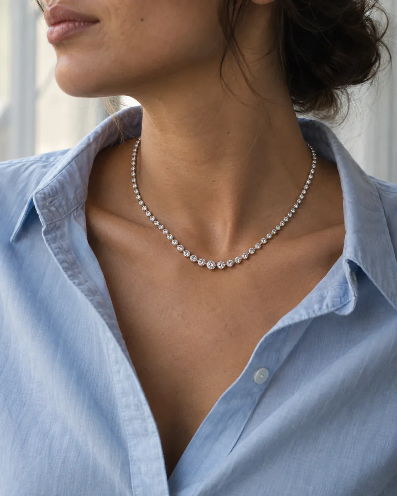 A white-gold graduated diamond necklace worn at the collar of a pale-blue cotton shirt.
